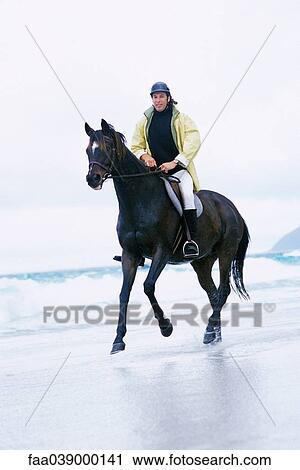 Stock Image - Man riding horse on beach. Fotosearch