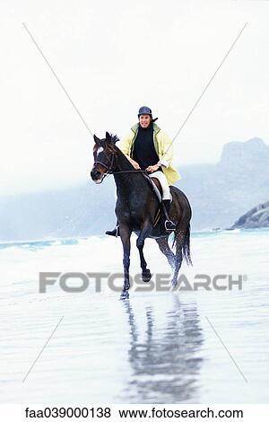 Stock Photo - Man riding horse on beach. Fotosearch