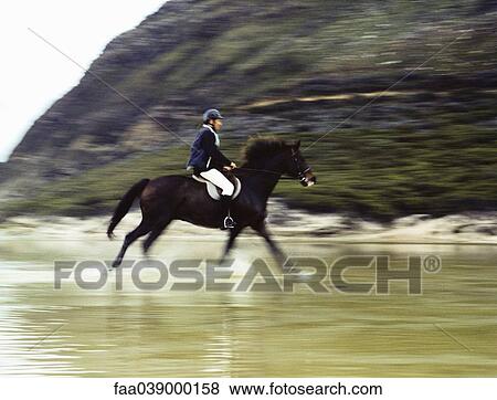 Stock Photo - Man riding horse through water, blurred motion. Fotosearch