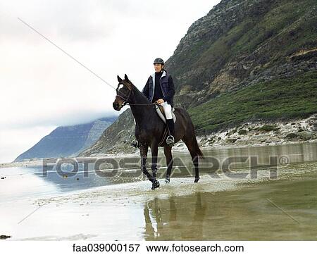 Stock Photo - Man riding horse through water. Fotosearch