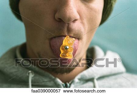 Stock Photo - Man sticking out pierced tongue, piercing holding candy bear. Fotosearch
