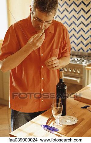 Picture - Men smelling cork of newly opened bottle of wine in kitchen. Fotosearch