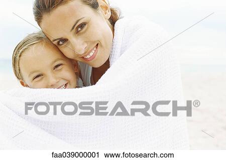 Stock Image - Mother and daughter wrapped in towel at the beach, portrait. Fotosearch