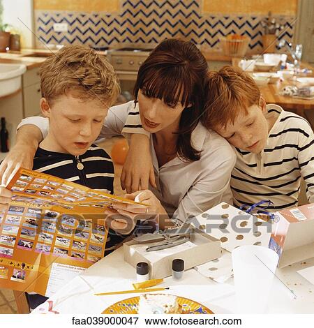 Stock Photo - Mother and son reading toy instructions after birthday party, second son leaning against mother. Fotosearch