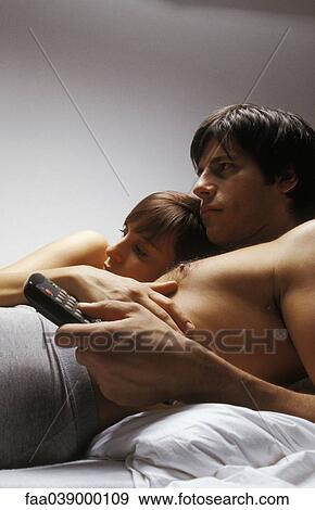 Stock Photo - Young couple lying together in bed watching television. Fotosearch