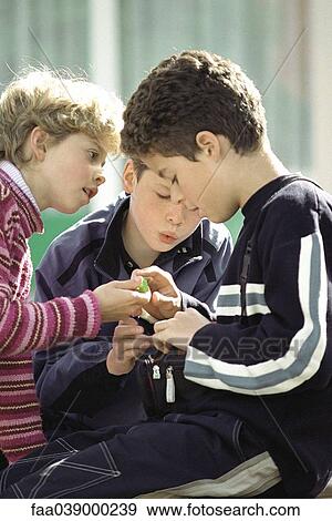Stock Photo - Young friends sitting together, looking at toy. Fotosearch