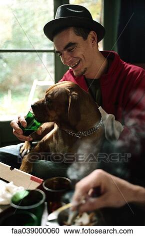 Stock Image - Young man letting pet dog drink from glass. Fotosearch