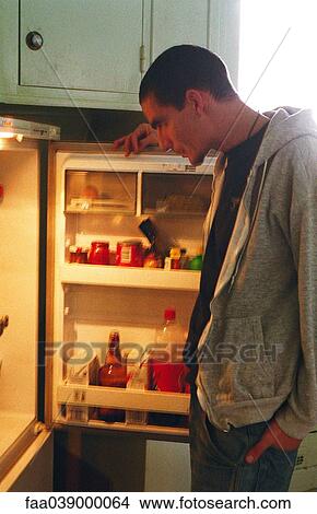 Picture - Young man standing in front of open refrigerator . Fotosearch