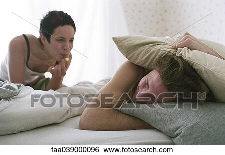 Stock Photograph - Young woman blowing whistle, awakening sleeping young man. Fotosearch
