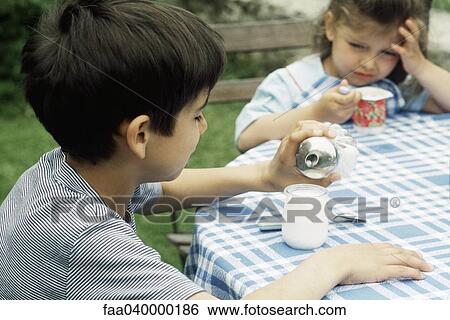 Boy sitting at table with sister, pouring sugar yogurt View Large Photo Image Stock Photograph - Boy sitting at table with sister, pouring sugar yogurt. Fotosearch