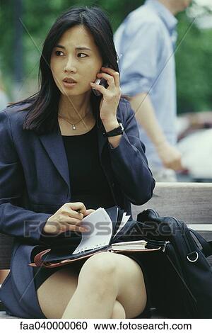 Businesswoman sitting on bench, using cell phone and flipping through agenda View Large Photo Image Stock Image - Businesswoman sitting on bench, using cell phone and flipping through agenda. Fotosearch