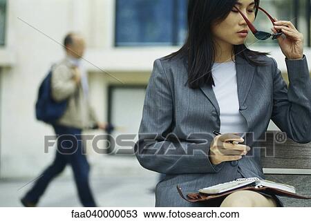 Businesswoman sitting on bench with agenda, putting on sunglasses View Large Photo Image Stock Image - Businesswoman sitting on bench with agenda, putting on sunglasses. Fotosearch