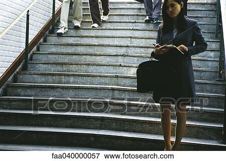 Businesswoman standing at bottom of steps, holding open agenda View Large Photo Image Stock Photo - Businesswoman standing at bottom of steps, holding open agenda. Fotosearch