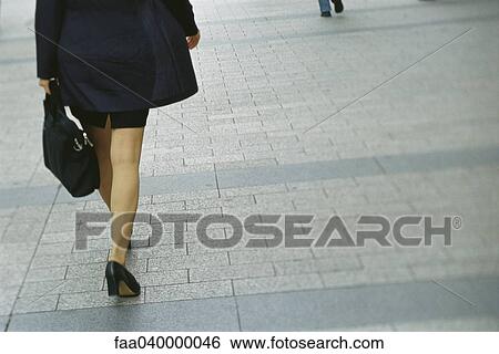 Stock Photograph - Businesswoman walking on sidewalk, rear view, cropped. Fotosearch