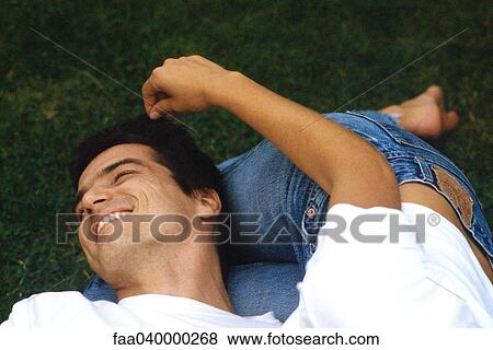 Stock Photo - Couple lying on ground, man's head resting on woman's legs. Fotosearch