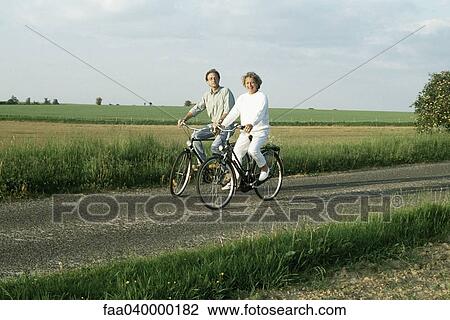 Couple riding bicycles through countryside, smiling at camera View Large Photo Image Stock Image - Couple riding bicycles through countryside, smiling at camera. Fotosearch