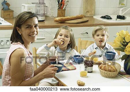 Family sitting at table for breakfast, smiling at camera View Large Photo Image Stock Image - Family sitting at table for breakfast, smiling at camera. Fotosearch