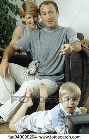 Picture - Family watching TV together, man pointing. Fotosearch
