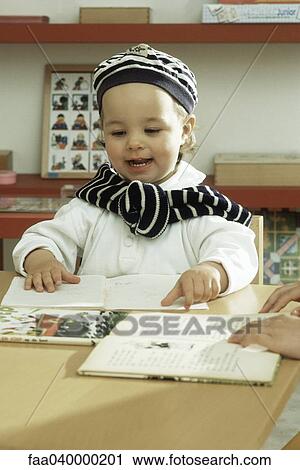 Little girl sitting at table, touching book View Large Photo Image Stock Image - Little girl sitting at table, touching book. Fotosearch