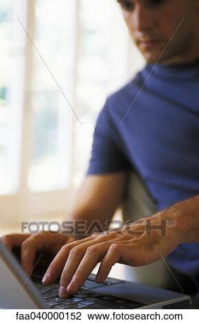 Stock Image - Man typing on laptop, focus on hands. Fotosearch