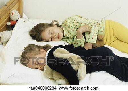 Sisters sleeping in bed, cuddling stuffed animals View Large Photo Image Picture - Sisters sleeping in bed, cuddling stuffed animals. Fotosearch