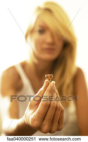 Stock Image - Woman holding ring, showing it to camera. Fotosearch