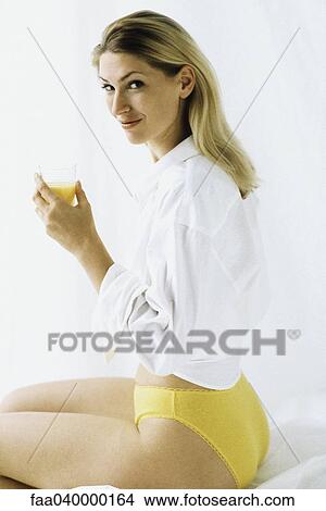 Woman in underwear holding cup of orange juice, smiling over shoulder at camera View Large Photo Image Picture - Woman in underwear holding cup of orange juice, smiling over shoulder at camera. Fotosearch