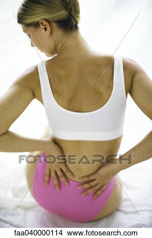 Woman sitting in underwear, holding lower back View Large Photo Image Picture - Woman sitting in underwear, holding lower back. Fotosearch