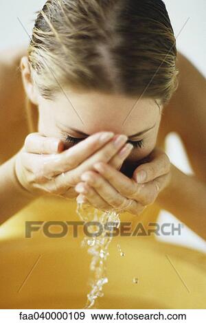 Stock Photo - Woman washing face in bathroom sink. Fotosearch