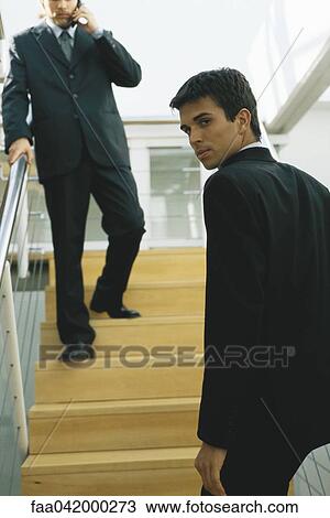 Stock Image - "Businessman going up steps, looking over shoulder at camera". Fotosearch