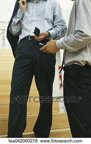 Stock Photo - "Businessmen standing together at foot of stairs looking at cell-phones, cropped view". Fotosearch