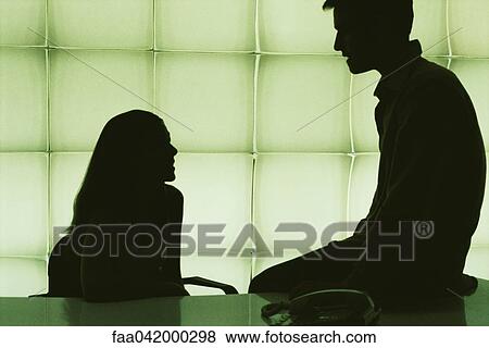 Stock Photo - "Colleagues chatting, man sitting on corner of desk, woman sitting at desk". Fotosearch