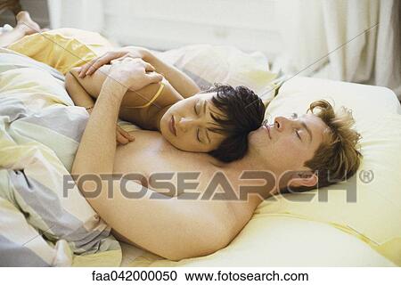 Stock Image - "Couple asleep in bed, woman's head resting on man's chest". Fotosearch