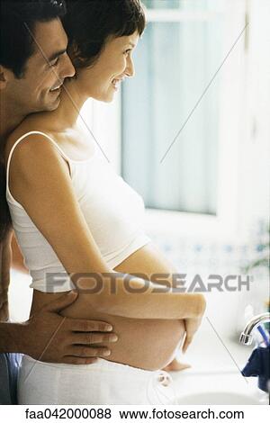 Stock Photo - "Couple embracing with hands on woman's pregnant stomach, side view". Fotosearch