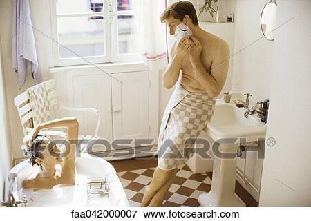 "Couple together in bathroom, woman bathing, man leaning against sink, shaving" View Large Photo Image Stock Photo - "Couple together in bathroom, woman bathing, man leaning against sink, shaving". Fotosearch