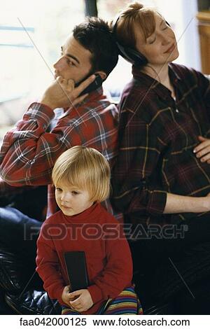 Stock Photography - "Family sitting back to back, father using cell phone, mother listening to headphones, daughter watching TV". Fotosearch