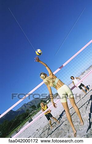 Stock Image - Female jumping to hit volleyball over net. Fotosearch