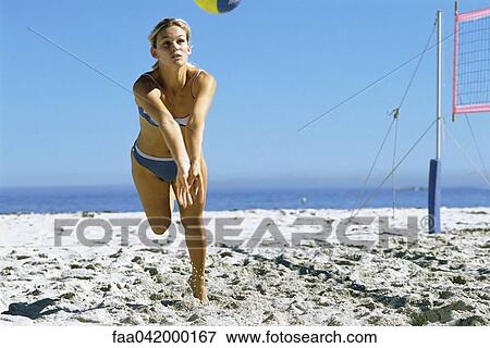 Stock Photo - Female playing beach volleyball running to catch ball. Fotosearch