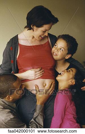 Stock Image - "Husband and children gathered around pregnant woman, smiling". Fotosearch