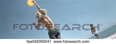 Stock Image - Male at beach jumping to catch frisbee. Fotosearch