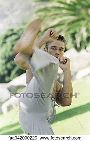 Stock Image - "Male practicing martial arts kick in park setting, front view". Fotosearch
