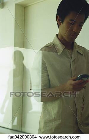 Picture - "Male text messaging, reflection of female in window". Fotosearch