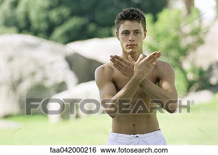Stock Photograph - "Male with arms raised, crossed, practicing martial arts in park setting". Fotosearch