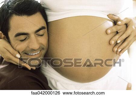 "Man embracing pregnant wife, resting his cheek on her stomach, cropped" View Large Photo Image Stock Photograph - "Man embracing pregnant wife, resting his cheek on her stomach, cropped". Fotosearch