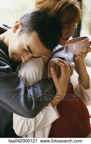 Stock Image - "Man embracing pregnant wife, woman drinking tea". Fotosearch