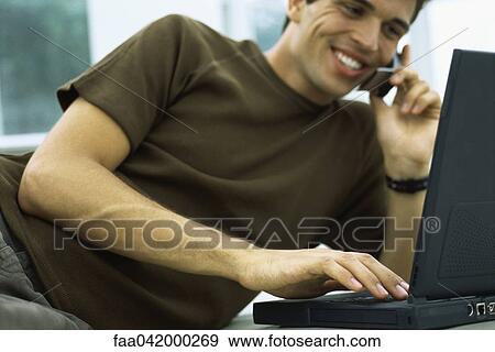 "Man leaning on elbow phoning, using laptop computer" View Large Photo Image Stock Photo - "Man leaning on elbow phoning, using laptop computer". Fotosearch
