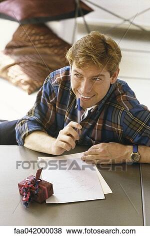 "Man sitting at table writing letter, gift nearby" View Large Photo Image Stock Photo - "Man sitting at table writing letter, gift nearby". Fotosearch