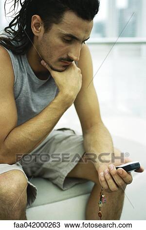 "Man sitting with hand under chin, looking at cell phone" View Large Photo Image Stock Image - "Man sitting with hand under chin, looking at cell phone". Fotosearch
