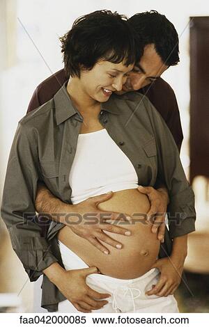 "Man standing behind pregnant wife, placing his hands on her bare stomach" View Large Photo Image Stock Photography - "Man standing behind pregnant wife, placing his hands on her bare stomach". Fotosearch