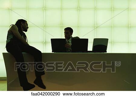 Man with dreadlocks sitting on desk leaning to side watching businessman using laptop computer View Large Photo Image Stock Image - Man with dreadlocks sitting on desk leaning to side watching businessman using laptop computer. Fotosearch